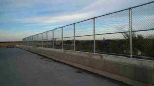 Tall, custom chain link railing atop cement wall. Grand Island fence company commercial fencing contractors Grand Island, Nebraska commercial industrial high security correctional recreational sport ballfield tennis court basketball pickleball football stadium track high school college playground manufacturing prison cell tower chain link barbwire gate posts tubing pipe top rail chain link fabric wire mesh galvanized aluminum vinyl coated black brown green 9 gauge fence fencing security perimeter razor concertina wire hinges installation repair costs panels hardware fittings 
